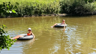 Zwei Menschen entspannen auf Schwimmreifen auf einem ruhigen Fluss, umgeben von grüner Natur.