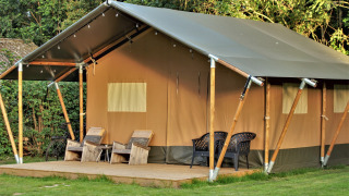 Tienda safari en Camping Gorishoek, Países Bajos, con terraza de madera, sillas y rodeada de árboles verdes.