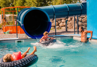 Børn leger i poolen foran en stor vandrutsjebane på Camping La Sténiole i Grand Est, Frankrig.