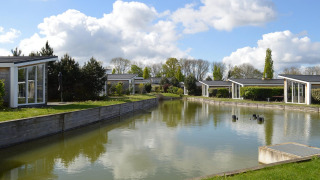 Cabañas modernas junto a un estanque en Resort Mooi Bemelen, Países Bajos, rodeadas de naturaleza y cielo.