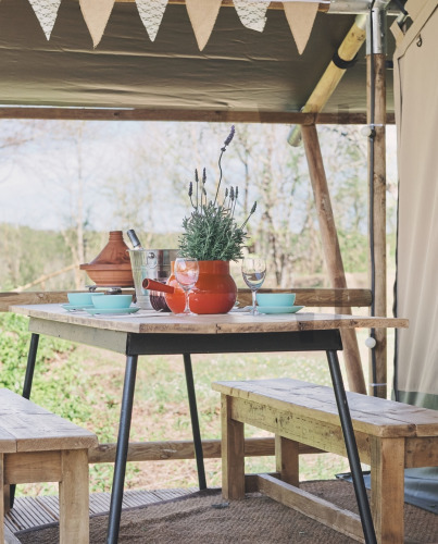 Mesa de madera rústica con bancos y lavanda en una tienda safari, preparada para una comida al aire libre.