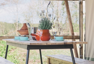 Houten picknicktafel met banken en lavendel in een safaritent, gezellig gedekt voor een maaltijd.