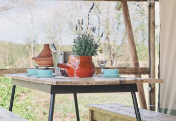 Houten picknicktafel met banken en lavendel in een safaritent, gezellig gedekt voor een maaltijd.