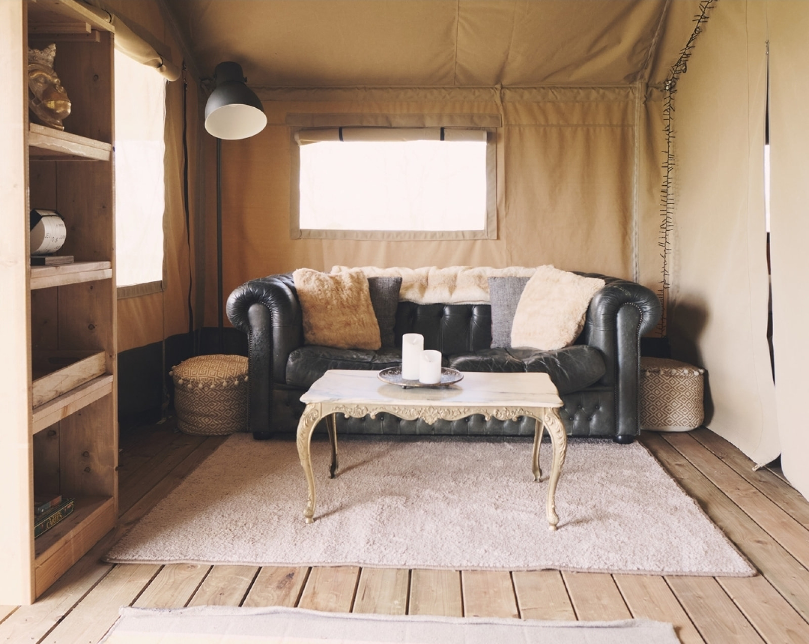 Stijlvolle safaritentinterieur met leren bank, houten vloer, zacht vloerkleed en decoratieve tafel.