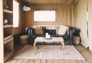 Intérieur de tente safari élégant avec canapé en cuir, table basse décorative et ambiance chaleureuse.