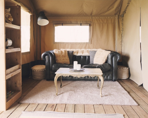 Intérieur de tente safari élégant avec canapé en cuir, table basse décorative et ambiance chaleureuse.
