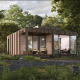 Et moderne træhus med store vinduer i skoven, omgivet af grønne træer og frodig vegetation.