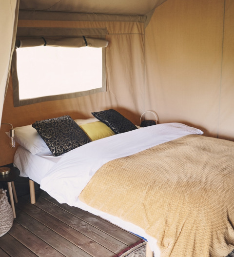 Knusse slaaphoek met dubbel bed, kussens en deken in een comfortabele safaritent met houten vloer.