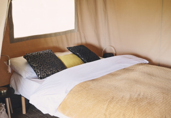 Acogedor dormitorio con cama doble, cojines y manta dentro de una elegante tienda safari de lujo.