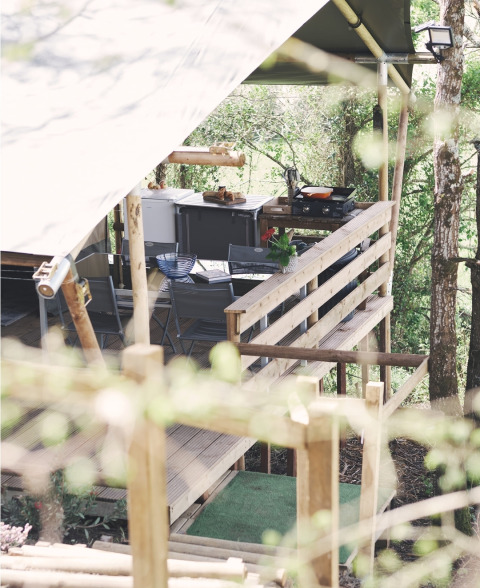 Vista laterale di una terrazza di tenda safari con cucina all'aperto e salotto tra gli alberi.