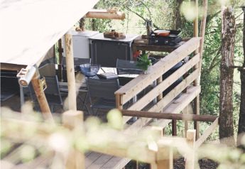Vista laterale di una terrazza di tenda safari con cucina all'aperto e salotto tra gli alberi.