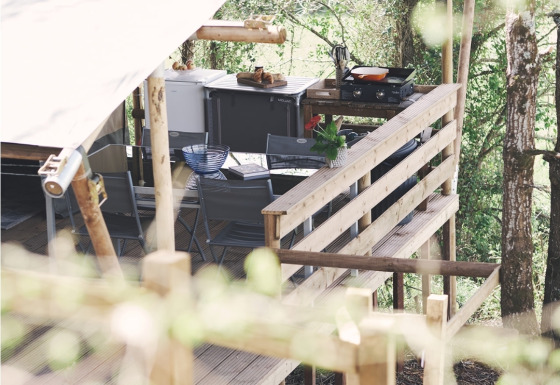 Vista laterale di una terrazza di tenda safari con cucina all'aperto e salotto tra gli alberi.