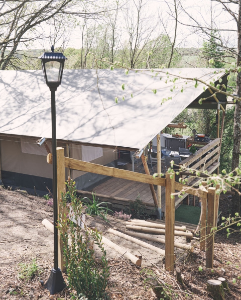 Safari-Zelt auf dem Camping d'Artagnan in Frankreich mit Holzterrasse, Stufen und Laterne im Grünen.