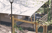Tienda safari en Camping d'Artagnan, Francia, con terraza de madera, escalones y farola rodeados de árboles.