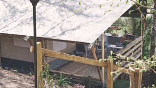 Safaritent op Camping d'Artagnan in Frankrijk met houten terras, traptreden en lantaarnpaal in het groen.