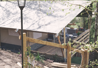 Safari tent at Camping d'Artagnan in France with wooden terrace, steps, and lamp post surrounded by trees.