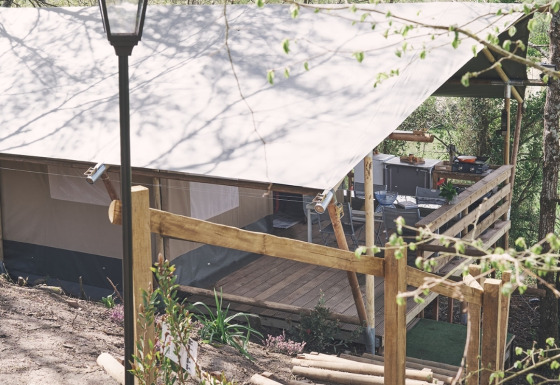 Safari tent at Camping d'Artagnan in France with wooden terrace, steps, and lamp post surrounded by trees.