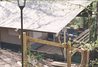 Safari-Zelt auf dem Camping d'Artagnan in Frankreich mit Holzterrasse, Stufen und Laterne im Grünen.