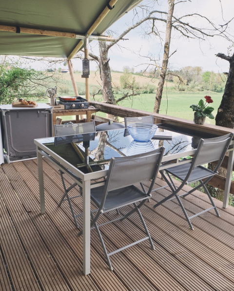 Espace repas extérieur sous tente safari au Camping d'Artagnan en France avec vue sur les champs verts.