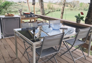 Espace repas extérieur sous tente safari au Camping d'Artagnan en France avec vue sur les champs verts.