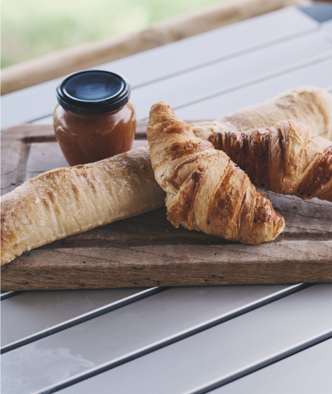 Frische Croissants und Baguette mit Marmeladenglas auf Holzbrett bei Safari Tent, Camping d'Artagnan, Frankreich.
