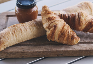 Friskbagte croissanter og brød med marmeladeglas på træbræt ved Safari Tent, Camping d'Artagnan, Frankrig.