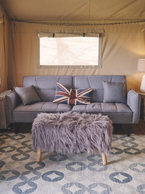 Indretning i safaritelt på Camping d'Artagnan i Frankrig med grå sofa, Union Jack pude og pelsbænk.