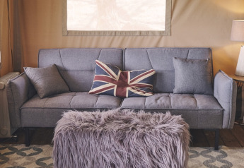 Intérieur de tente safari au Camping d'Artagnan en France avec canapé gris, coussin Union Jack et banc en fourrure.