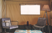 Knusse zithoek in een safaritent op Camping d'Artagnan in Frankrijk, met stoelen, tafel en sfeerverlichting.