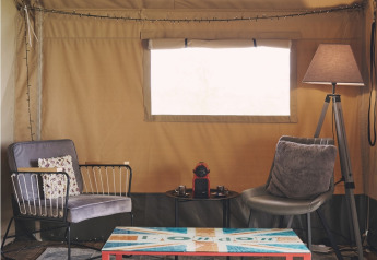 Coin salon confortable dans une tente safari au Camping d'Artagnan en France, avec fauteuils et table colorée.