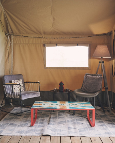 Coin salon confortable dans une tente safari au Camping d'Artagnan en France, avec fauteuils et table colorée.