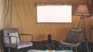 Coin salon confortable dans une tente safari au Camping d'Artagnan en France, avec fauteuils et table colorée.