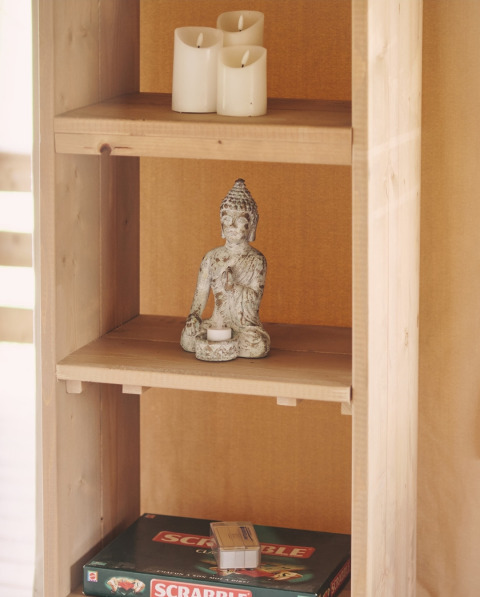 Træhylde i en safaritelte med Buddha-figur, batteridrevne stearinlys og Scrabble-spil i Frankrig.