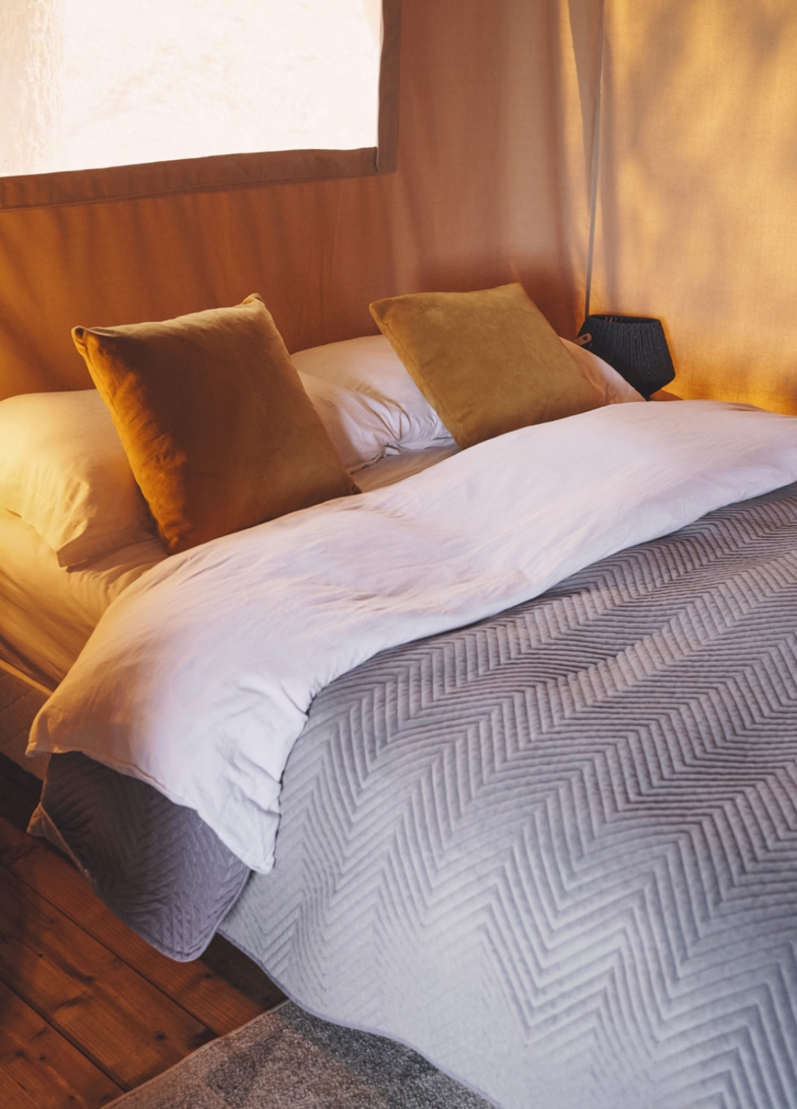 Knus bed met okergele kussens in een safaritent op Camping d'Artagnan in Frankrijk.
