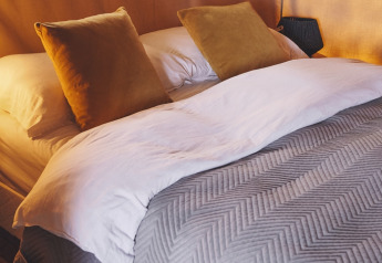 Letto accogliente con cuscini senape in una tenda safari al Camping d'Artagnan in Francia.