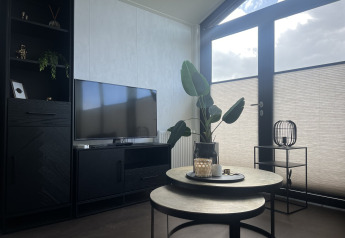 Modernes Wohnzimmer im Chalet Sea Pearl im Vakantiepark de Zeeuwse Parel mit TV, Tisch und Pflanze.