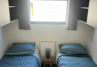 Habitación con dos camas individuales, ropa de cama azul, ventana y cortinas oscuras en Zeeuwse Parel.