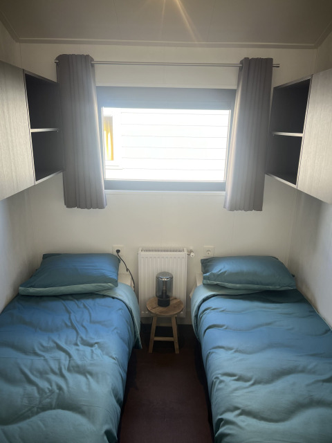 Habitación con dos camas individuales, ropa de cama azul, ventana y cortinas oscuras en Zeeuwse Parel.