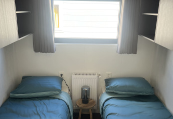 Habitación con dos camas individuales, ropa de cama azul, ventana y cortinas oscuras en Zeeuwse Parel.