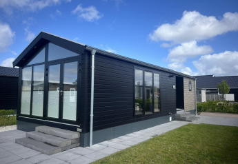 Chalet moderno llamado Sea Pearl con grandes ventanales, fachada negra y terraza pavimentada bajo cielo azul.