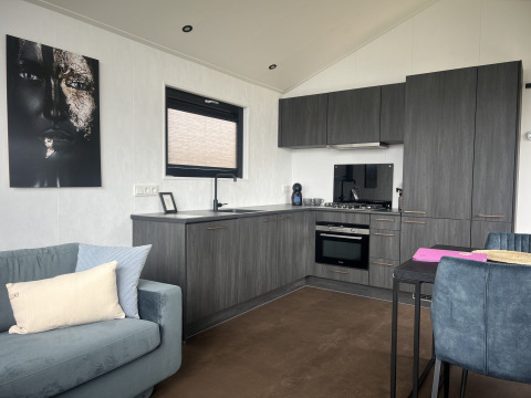 Cocina y sala modernas en chalet con sofá azul y arte en la pared en Sea Pearl de Vakantiepark de Zeeuwse Parel, Países Bajos.