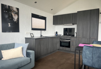 Interno di chalet moderno con cucina grigia, divano blu e arte murale al Sea Pearl nel Vakantiepark de Zeeuwse Parel, Paesi Bassi.