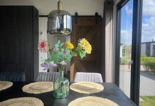 Solrigt spiseområde i Sea Pearl-chalet, Vakantiepark de Zeeuwse Parel, Holland, med blomster og lys.