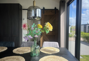 Solrigt spiseområde i Sea Pearl-chalet, Vakantiepark de Zeeuwse Parel, Holland, med blomster og lys.