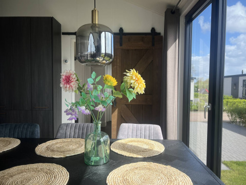 Dining area in Sea Pearl chalet at Vakantiepark de Zeeuwse Parel, Netherlands, with flowers and sunlight.