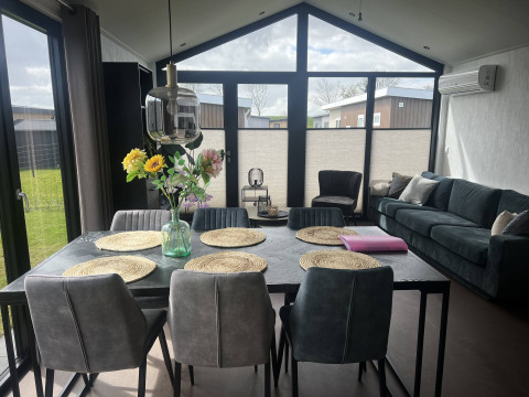 Moderne stue og spisestue med store vinduer i Sea Pearl-chalet på Vakantiepark de Zeeuwse Parel, Holland.