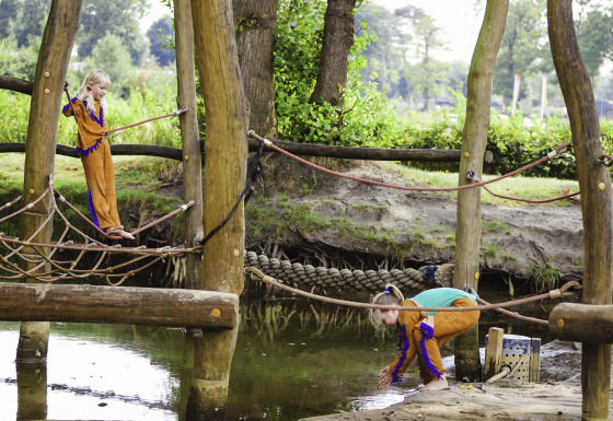 Children play on a wooden adventure playground with ropes and water at Beloofde Land in Gelderland, Netherlands.