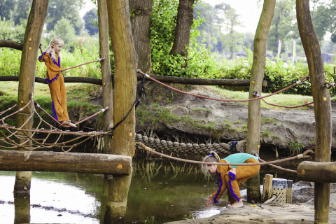 Kinderen spelen op een houten avonturenspeeltuin met touwen en water in Beloofde Land, Gelderland.
