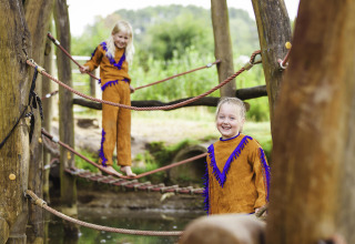 To børn i farverige jakkesæt leger på en reb-bro i Beloofde Land feriepark i Gelderland, Holland.