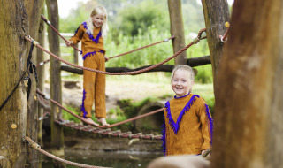 Dos niños con disfraces juegan sobre un puente de cuerda en el parque Beloofde Land, Gelderland, Países Bajos.